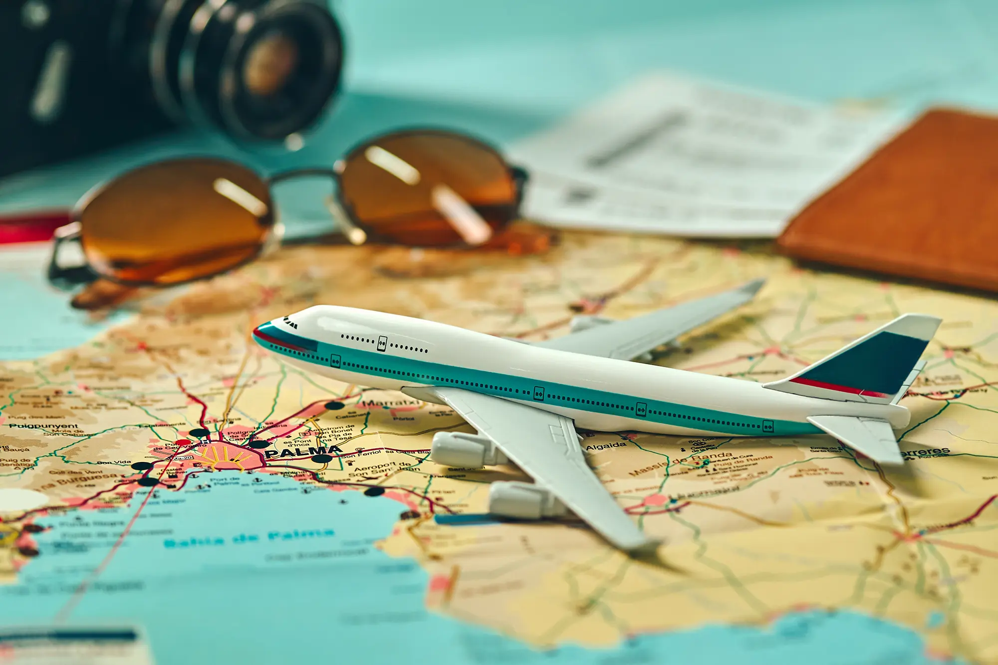 A small replica of an airplace on a map with a passport and sunglasses nearby